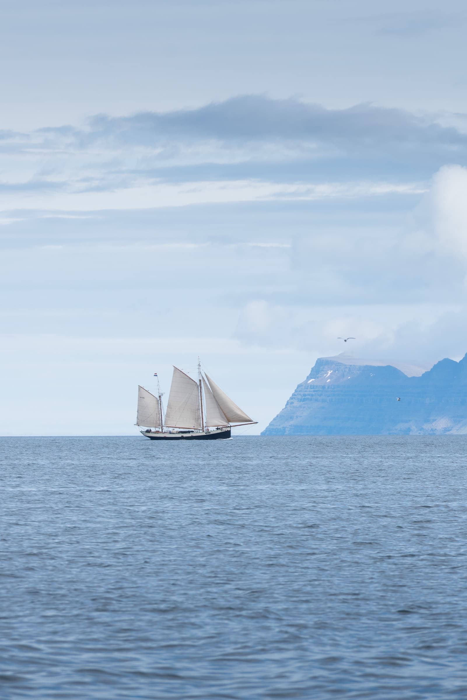 Seglskip á lygnum sjó fyrir framan fjöll