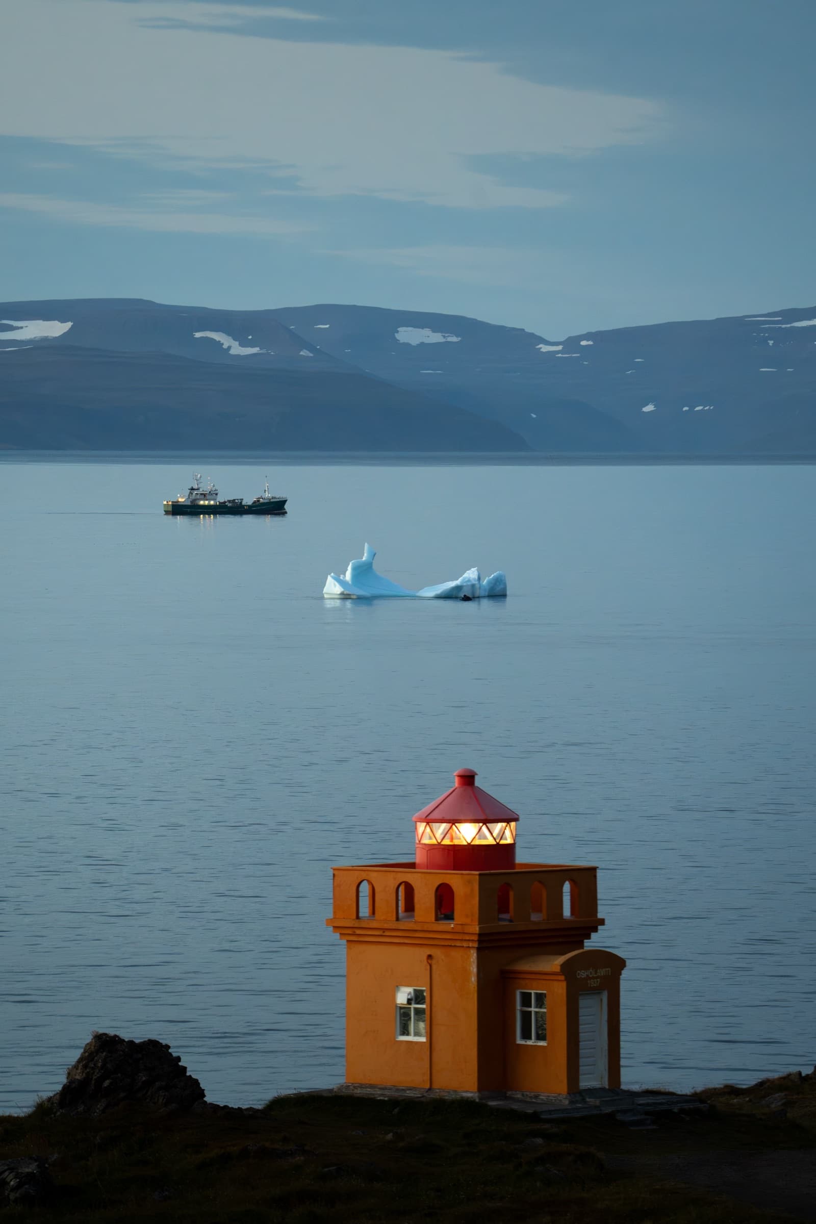 Rauður viti, borgarísjaki og bátur í firðinum